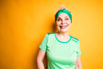 Cheerful woman in sportswear smiling broadly while standing on yellow background and going to the gym
