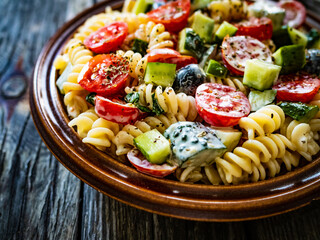 Pasta with fresh vegetables and black olives on wooden table
