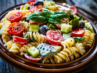 Pasta with fresh vegetables and black olives on wooden table
