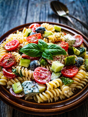 Pasta with fresh vegetables and black olives on wooden table
