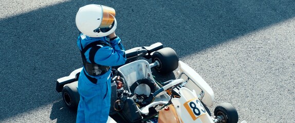 Teenager professional karting racer putting on protective gear on a race track - obrazy, fototapety, plakaty