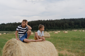 Naklejka na ściany i meble little caucasian adorable boys sitting on haysack in a field on summer time with straw in mouth. Karelia region of Russia