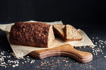 Bread with sunflower and flax seeds on a wooden cutting board on a black background