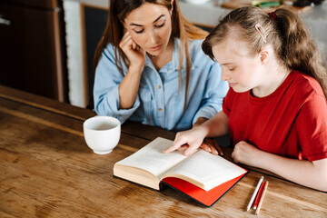 White woman helping her daughter with down syndrome reading book