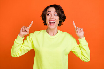 Photo of young cheerful happy woman look empty space point finger ad isolated on orange color background
