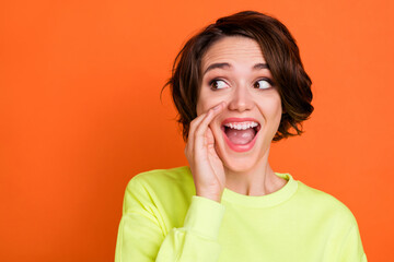 Portrait of attractive cheerful girl saying good news copy space advert isolated over bright orange color background