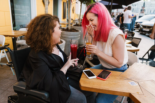 Young two women laughing and drinking cocktails while sitting in cafe