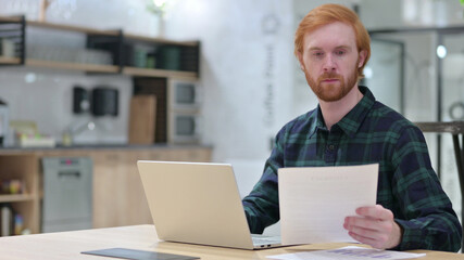 Redhead Man with Laptop Working on Documents 