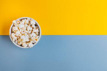 White bowl with popcorn on blue and yellow background.