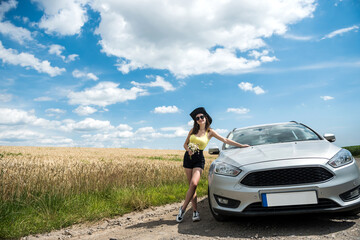 portrait of young beautiful woman standing near her car at rural road