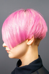 Profile portrait of a young caucasian woman with pink bob haircut isolated on a gray background