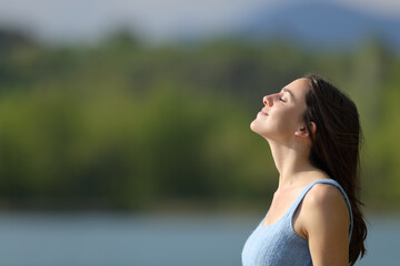 Relaxed woman breathing fresh air meditating beside a lake - obrazy, fototapety, plakaty