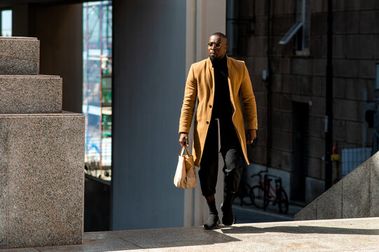 Black handsome man in elegant stylish clothing walking in hurry holding a bag. City life and urban lifestyle.