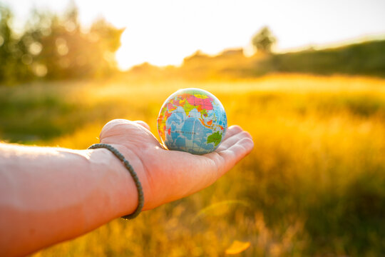 Men's hands hold a globe at sunset in the park. The concept of environmental protection