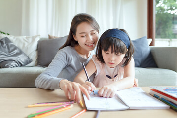 Asian mother teaching her cute kid daughter to studying in living room at home