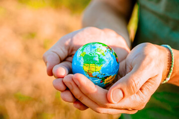 Men's hands hold a globe at sunset in the park. The concept of environmental protection