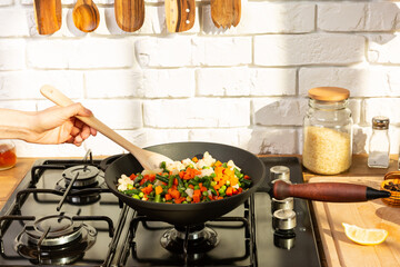 Woman cooks vegetarian dinner  in a pan on gas plate