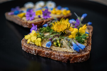 vegan cream cheese substitute on a whole grain bread slice or toast which is flowery decorated with Red clover, dandelion and meadow flowers for a healthy breakfast or snack