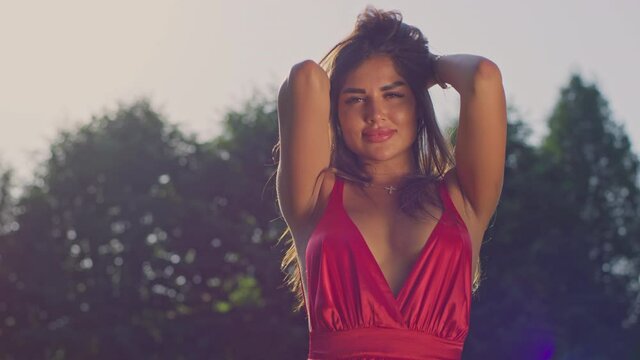 The girl is a model in a red dress. Brunette and sunset. Looks at the camera