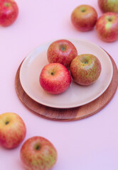 In the vertical photo, ripe apples are lying in a pink dessert plate on a pink background