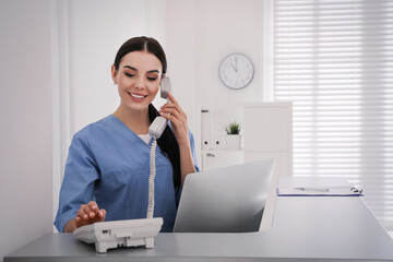 Receptionist talking on phone at countertop in hospital, space for text