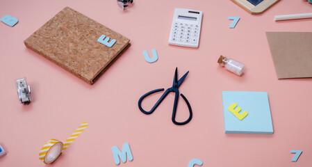 Back to school creative concept. Colorful pattern of vibrant foam letters, scissors, calculator and other stationery in a chaotic manner lying on pink paper background. Flat lay.