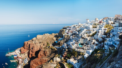 Fototapeta na wymiar Santorini, Greece. Panoramic view of traditional houses in Santorini. Small narrow streets and rooftops of houses, churches and hotels. Oia village, Santorini Island, Greece. Travel and vacation photo