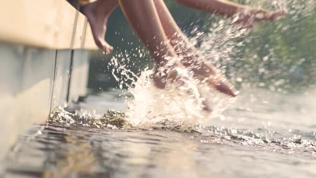 Legs in water. Children sitting on pier and having fun. Splashing water close up.