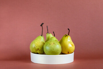 green fresh pears on white podium against brown background
