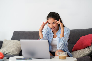 Funny amazed casual latin woman at home looking to her laptop and jawdropping.
