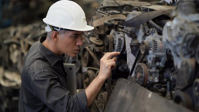 senior engineer using laptop computer checking list old used car engine in machinery parts shop warehouse. old technician man Repair vehicle automobile machine in Recycle motor factory