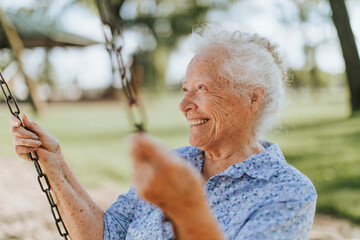 Cheerful senior woman on a swing at a playground - obrazy, fototapety, plakaty