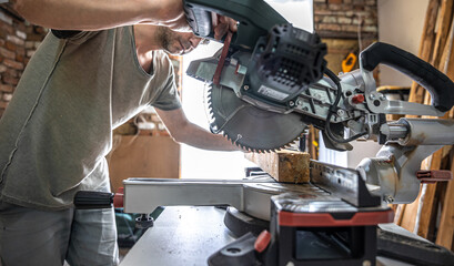 Professional carpenter working with a miter saw. - obrazy, fototapety, plakaty