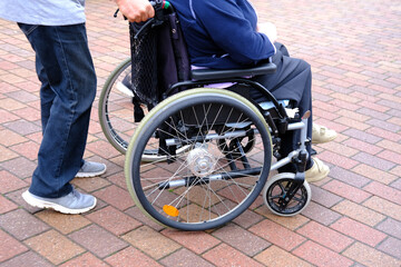 Obraz premium male nurse in park is driving elderly woman of 70-75 years old European Caucasian appearance in wheelchair, concept of care for skinny people, life of sedentary people with disabilities, paralysis