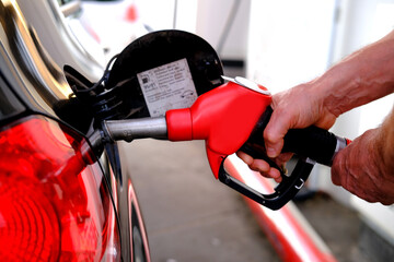 close-up male hand holding a red refueling gun, refueling a car with an internal combustion engine...