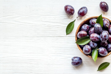 Ripe garden plums in bowl. Cherry fruit with leaves. Top view