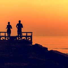 Healthy young couple running by the beach together in a sunset