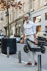 smiling middle aged man in white shirt carrying electric scooter on street