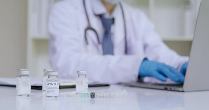 Covid-19 vaccine on the desk with hands of doctor typing on notebook computer for register the patient data to network behide,