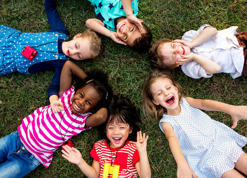 Group of kindergarten kids lying on the grass at park and relax with smiling