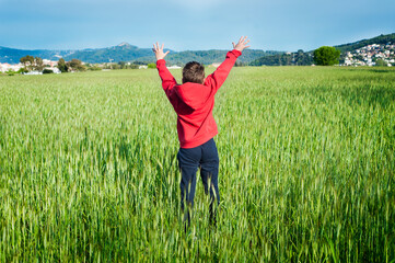 Un niño con una sudadera roja salta en medio de un campo de trigo.