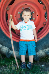 Un niño de pie con un bastón con una rueda de tractor detrás.