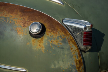 Chromium plated rear lamp of a green classic car before restoration. Photo taken in natural light.