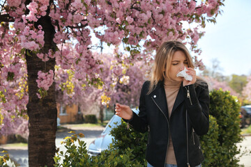 Woman suffering from seasonal pollen allergy near blossoming tree outdoors - obrazy, fototapety, plakaty