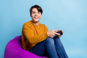 Photo of funky brunet millennial guy sit on bag playstation wear sweater jeans isolated on blue color background