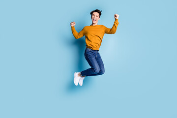 Full size photo of funny brunet millennial guy jump wear sweater jeans isolated on blue color background