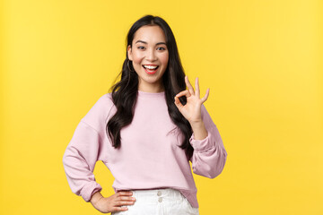People emotions, lifestyle and fashion concept. Impressed and excited smiling asian woman totally agree with you, showing okay sign and nod approval, standing yellow background - obrazy, fototapety, plakaty