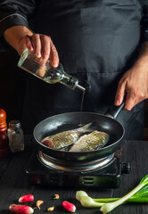 Professional chef prepares fresh fish in pan with oil. Preparation for cooking fish food. Working environment in the kitchen of a restaurant or cafe.