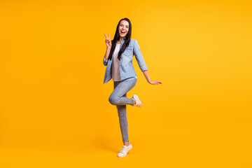 Fototapeta na wymiar Full size photo of nice optimistic brunette lady show v-sign wear blue shirt jeans sneakers isolated on yellow color background