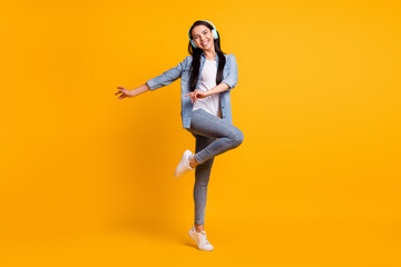 Fototapeta na wymiar Full size photo of cool optimistic brunette lady listen music dance wear blue shirt jeans sneakers isolated on yellow color background
